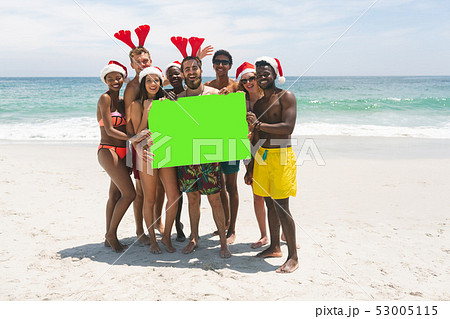 Multi-ethnic group of friends holding a empty green placard at beach on a sunny day 53005115