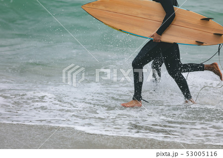 Male friends walking on beach while holding surfboard Male friends walking on beach while holding surfboard 53005116