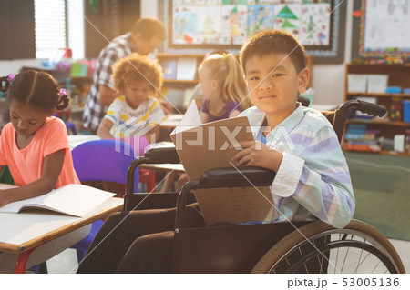 Schoolboy looking at camera while sitting at desk in school Schoolboy looking at camera while sitting at desk in school 53005136