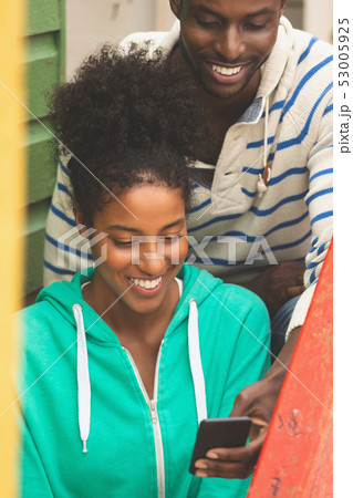 Couple using mobile phone while sitting near beach hut Couple using mobile phone while sitting near beach hut 53005925