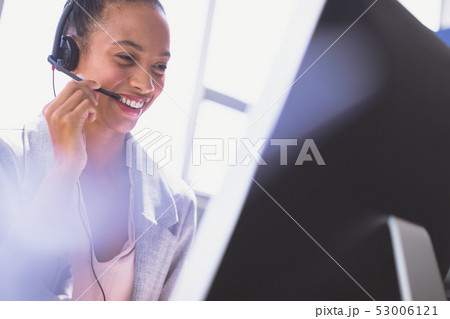 Businesswoman talking on headset while working on computer at desk Businesswoman talking on headset while working on computer at desk 53006121
