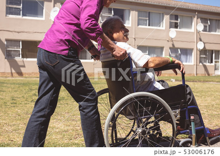 Senior woman pushing senior man on wheelchair at nursing park Senior woman pushing senior man on wheelchair at nursing park 53006176