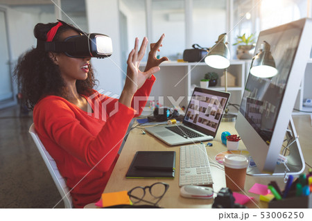 Female graphic designer using virtual reality headset at desk  53006250