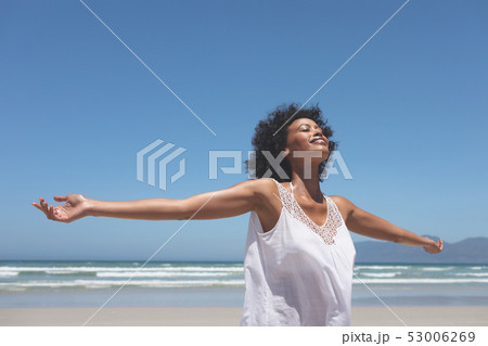 Beautiful woman standing with open arm at beach on sunny day 53006269