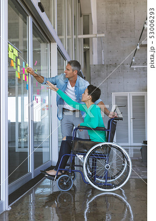 Business people discussing over sticky notes on glass wall in office Business people discussing over sticky notes on glass wall in office 53006293