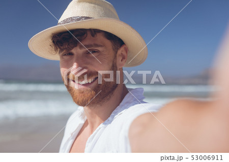 Man standing at beach while holding camera Man standing at beach while holding camera 53006911