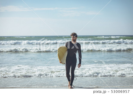 Male surfer with a surfboard walking on a beach 53006957