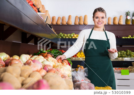 female seller in apron offering fresh greens and vegetables 53010399