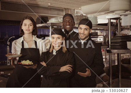 Woman waiter with command of cooks are posing together on kitche Woman waiter with command of cooks are posing together on kitche 53010627