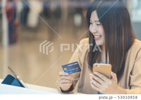 Asian woman using credit card with mobile phone for online shopping in department store over the clothes shop store background, technology money wallet and online payment concept, credit card mockup 53010958