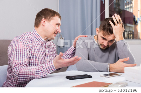 Friend calming distressed guy at home table Friend calming distressed guy at home table 53012196
