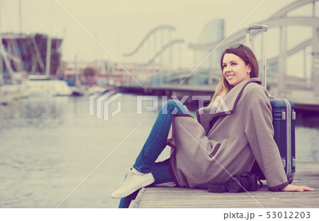 woman with luggage posing at quay and smiling 53012203