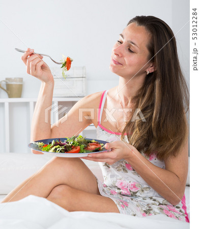 Woman in nightgown coat eats salad in bed Woman in nightgown coat eats salad in bed 53012284