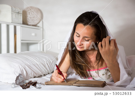Adult woman writing in diary and laying in bed at night Adult woman writing in diary and laying in bed at night 53012633