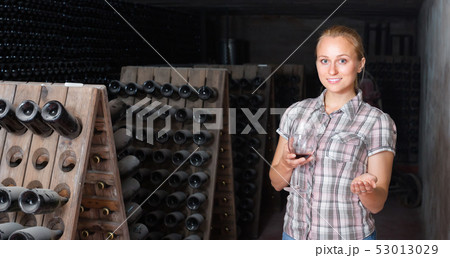 woman holding glass of wine in cellar. 53013029