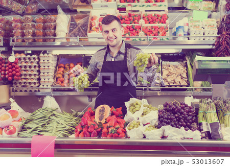attentive male seller showing assortment of grocery shop attentive male seller showing assortment of grocery shop 53013607