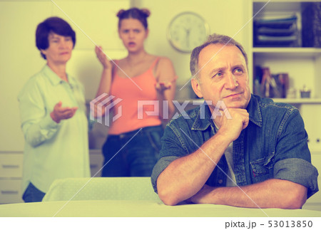 Woman and her daughter are sympathying their sad father who is sitting at the table 53013850