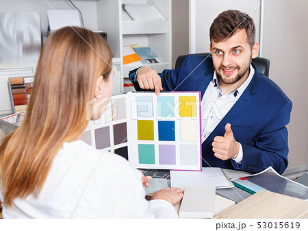 Competent seller in showroom helping young female client to choose furniture materials for her apartment 53015619