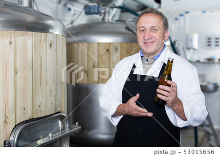 Portrait of brewer who is standing with bottle for beer on his workplace 53015656