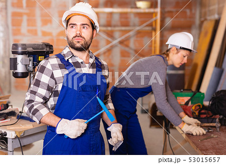 Portrait of two confident workers in uniform with tools inside brick cottage 53015657