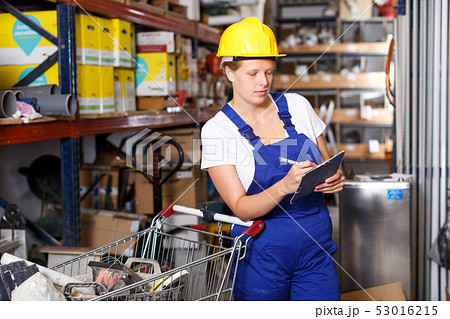 Young woman customer in helmet with notebook looking construction materials Young woman customer in helmet with notebook looking construction materials 53016215