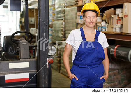 Young woman worker in helmet standing near car and shelves in warehouse Young woman worker in helmet standing near car and shelves in warehouse 53016216