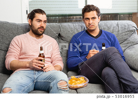 Two men watching matchup on tv with shouts of joy while drinking beer together at home Two men watching matchup on tv with shouts of joy while drinking beer together at home 53016955