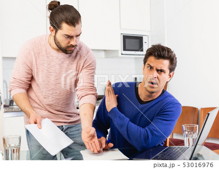 Man having problems with some documents; worriedly discussing with friend at home table Man having problems with some documents; worriedly discussing with friend at home table 53016976