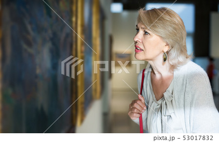 Mature woman standing in art museum near the painting in baguette Mature woman standing in art museum near the painting in baguette 53017832