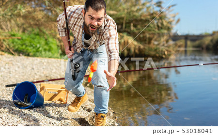 Adult man standing near river and pulling fish expressing emotions of dedication 53018041