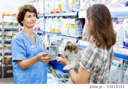 Elderly female veterinarian recommending pet food to young woman visiting pet store with her puppy 53019161