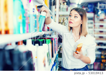 Portrait of surprised young woman near shelves with hair care products at cosmetics store Portrait of surprised young woman near shelves with hair care products at cosmetics store 53019413