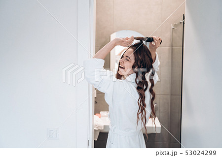 Beautiful smiling woman curling long hair using curling iron. 53024299