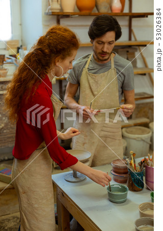 Smart dark-haired master holding brushes and talking to young student 53026384