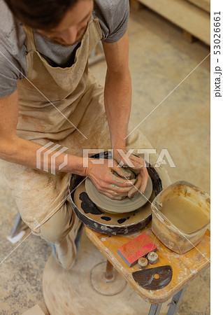 Hard-working skilled guy sitting on a wooden bench with pottery wheel 53026661