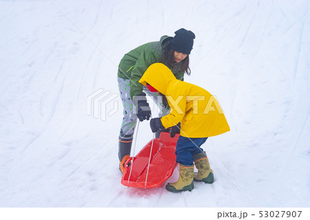 Mother is helping her daughter to ride the sled Mother is helping her daughter to ride the sled 53027907