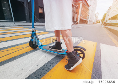 The girl on the electric kick scooter at a pedestrian crossing, legs close-up 53028836
