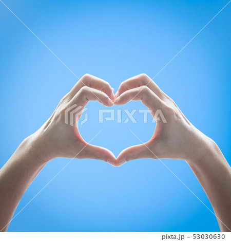 Heart shape woman hand raising against blue sky 53030630