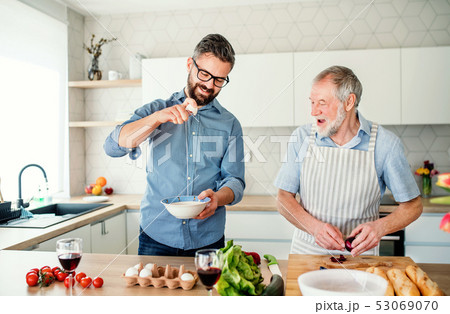An adult hipster son and senior father indoors at home, cooking. An adult hipster son and senior father indoors at home, cooking. 53069070