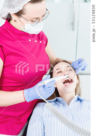 A professional dentist woman in glasses and overalls examines the oral cavity of a young girl in the 53129830