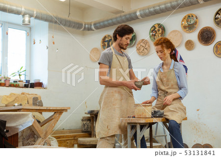Attentive ginger curly girl sitting on pottery equipment 53131841