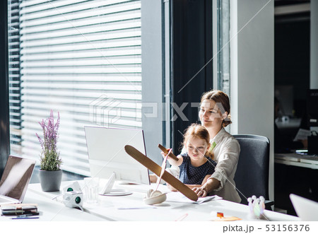 A businesswoman with small daughter sitting in an office, working and playing. A businesswoman with small daughter sitting in an office, working and playing. 53156376