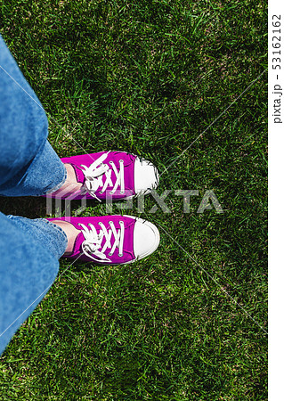 Legs in old pink sneakers on green grass. View 53162162