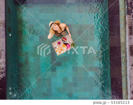 Breakfast tray in swimming pool, floating breakfast in luxury hotel. Girl relaxing in the pool Breakfast tray in swimming pool, floating breakfast in luxury hotel. Girl relaxing in the pool 53165213