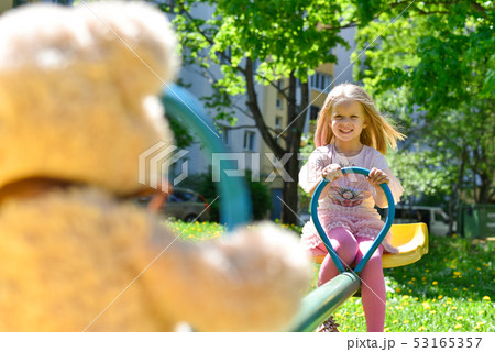 Cheerful girl riding on a swing with a toy bear Cheerful girl riding on a swing with a toy bear 53165357
