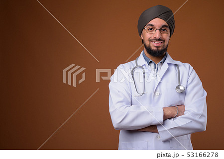 Young bearded Indian Sikh man doctor wearing turban against brow Young bearded Indian Sikh man doctor wearing turban against brow 53166278