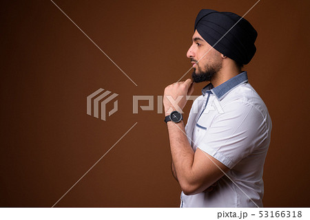 Young bearded Indian Sikh man wearing turban against brown backg 53166318