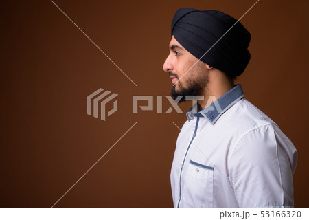 Young bearded Indian Sikh man wearing turban against brown backg 53166320