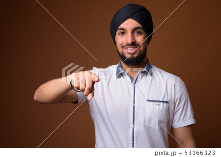 Young bearded Indian Sikh man wearing turban against brown backg Young bearded Indian Sikh man wearing turban against brown backg 53166323