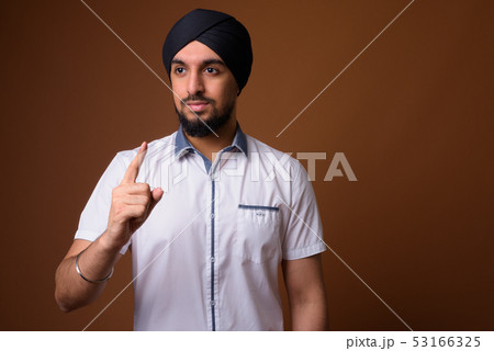 Young bearded Indian Sikh man wearing turban against brown backg 53166325